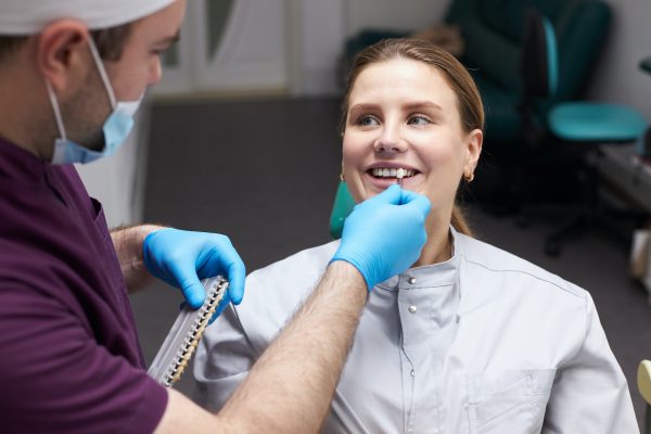 doctor-checks-the-color-of-tooth-according-to-the-comparative-scale-of-veneers-woman-at-the-dentist.jpg
